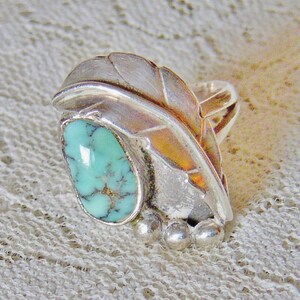 May include: A silver ring with a turquoise stone set in a leaf design. The ring has three small silver balls on the band.