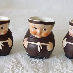 Puede incluir: Tres tazas de cerámica con forma de monjes con túnicas marrones y caras blancas. Las tazas tienen un borde y un asa blancos.