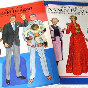 May include: Two paper doll books by Tom Tierney. The left book features Ronald Reagan in various outfits, including a suit and pajamas with a chimpanzee. The right book features Nancy Reagan in formal attire, including a red skirt and a white gown.