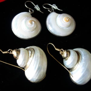 May include: Four earrings with a seashell design. Two pairs of earrings are visible. One pair has a spiral design, and the other pair has a layered design. The earrings have silver and gold accents and are set against a black background.