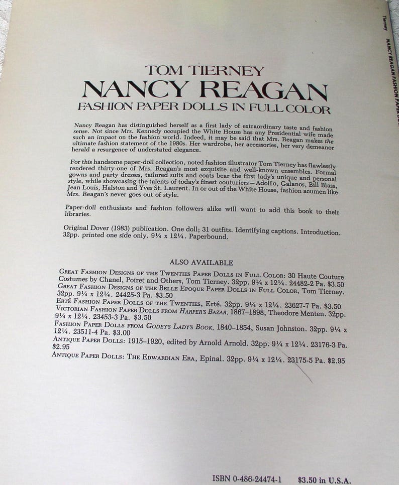 May include: A paperbound book titled Tom Tierney Nancy Reagan Fashion Paper Dolls in Full Color. The cover features black text on a cream background, detailing the collection of one doll and 31 outfits, measuring 9.25 inches by 12.25 inches.