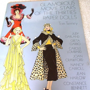 May include: A softcover book titled GLAMOROUS MOVIE STARS OF THE THIRTIES PAPER DOLLS by Tom Tierney. The light blue cover features illustrations of three figures in vintage attire, including a yellow gown and a leopard print coat, with names listed.