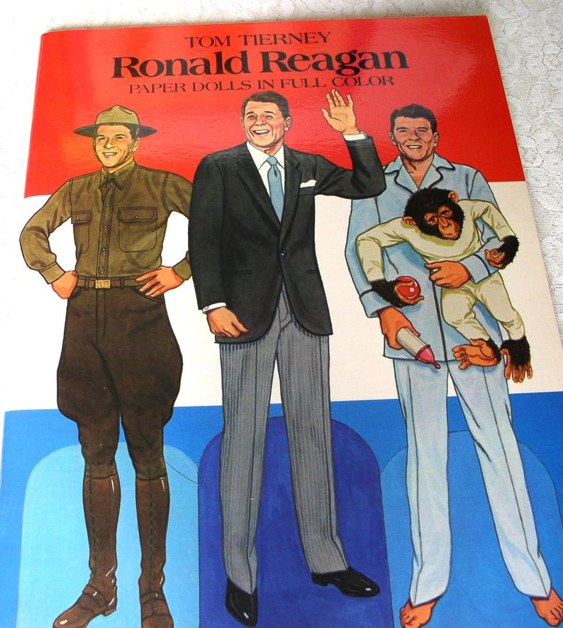 May include: A Tom Tierney Ronald Reagan Paper Dolls in Full Color book cover featuring three illustrations of Ronald Reagan in different outfits: a brown military uniform, a black suit with grey trousers, and light blue pajamas holding a chimpanzee.