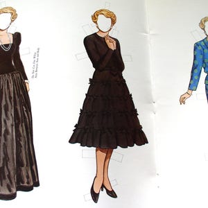 May include: Three paper dolls with blonde hair and blank faces. The first wears a black long-sleeved gown with a full skirt and pearl necklace. The second wears a black dress with a tiered ruffled skirt. The third wears a blue suit with green patterns.