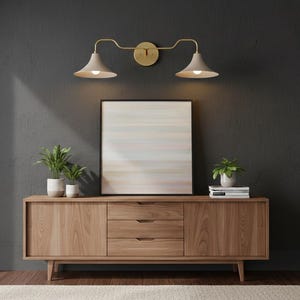 Può includere: Un mobile in legno in stile moderno di metà secolo, con tre cassetti e due ante. Il mobile è adornato da un'opera d'arte astratta incorniciata, piante in vaso e libri. Un'applique in ottone con due paralumi è montata sulla parete grigio scuro.