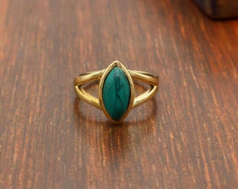 Puede incluir: Un anillo de tono dorado con una piedra turquesa central en forma de marquesa con vetas oscuras. La banda metálica se divide en dos brazos finos y lisos que se unen en los extremos puntiagudos del engaste de la piedra.