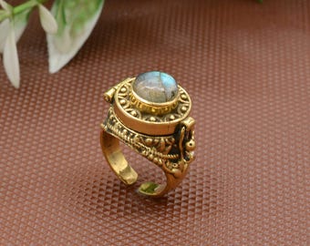 Puede incluir: Un anillo de metal dorado con una banda texturizada y ornamentada y una parte superior circular tipo relicario. El relicario tiene engastada una piedra de labradorita redonda e iridiscente con destellos azules y grises. Diseño abierto ajustable.