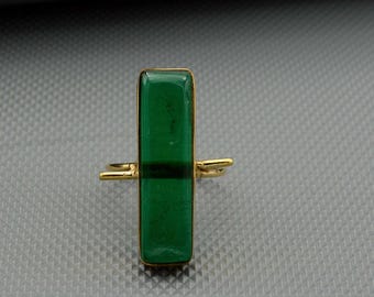 Puede incluir: Un anillo de oro con una piedra rectangular de color verde esmeralda con una franja verde oscuro. El anillo tiene un diseño minimalista con una banda dorada y un engaste rectangular. Es una joya.