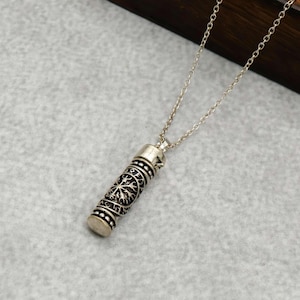 May include: Silver pendant necklace with a cylindrical pendant. The pendant has an intricate tree-like design. The necklace features a delicate chain and decorative top and bottom elements.