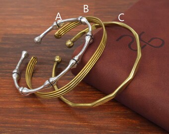 Puede incluir: Tres brazaletes de metal etiquetados A, B y C. El brazalete A es un brazalete plateado con un diseño segmentado similar al bambú. El brazalete B es un brazalete dorado con tres bandas finas paralelas. El brazalete C es un brazalete circular dorado liso.