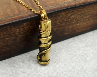 Puede incluir: Collar con colgante dorado con un diseño cilíndrico y una serpiente enrollada. El colgante cuelga de una delicada cadena dorada. El collar se muestra sobre un fondo de madera.