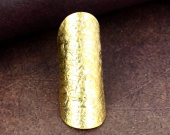 Puede incluir: Un anillo dorado con una superficie texturizada. El anillo tiene una forma ovalada alargada y está hecho de un material metálico brillante. Esta joya es una pieza de joyería.
