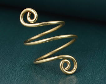 Puede incluir: Un anillo de metal en tono dorado con un diseño de espiral continua. La banda forma una bobina que se enrolla, terminando en dos bucles circulares en la parte superior e inferior. La superficie del metal tiene un acabado liso y pulido.
