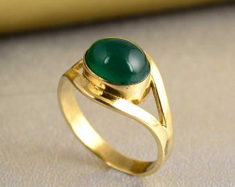Puede incluir: Un anillo de oro con una gran gema ovalada de color verde oscuro. La banda del anillo tiene un diseño dividido, con un acabado liso y pulido. La gema está engastada en un bisel.