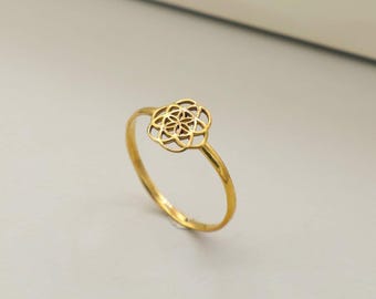 Puede incluir: Un anillo de tono dorado que presenta un delicado motivo circular calado en la banda. La pieza central consiste en un patrón geométrico de círculos superpuestos, creando un diseño simétrico similar a una flor de metal pulido.