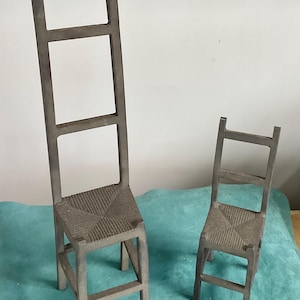 May include: Two gray miniature chairs with woven seats. One chair is tall and narrow, resembling a ladder-back design, while the other is a standard chair size. Both have a rustic, aged appearance, suggesting they are decorative items.