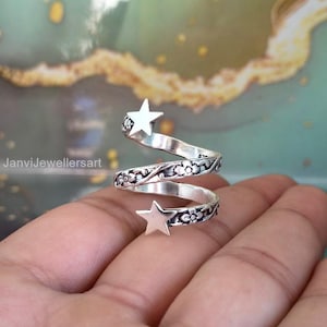 May include: A silver spiral ring with two star accents. The ring features a floral design along the band and the text "JanviJewellersart". The ring is a unique piece of jewelry.
