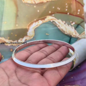 May include: A silver bangle bracelet with a flat, polished surface. The bracelet is round and appears to be made of metal. The text "JanviJewellersart" is visible in the image.