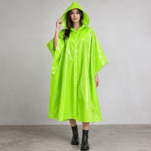 May include: A bright neon green hooded raincoat with a glossy, smooth finish. This waterproof garment features a loose, flowing silhouette, a pointed hood, and a central vertical button closure that extends from the neckline to the hemline.