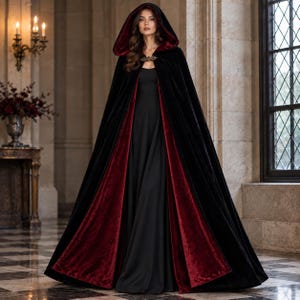 Puede incluir: Una capa con capucha que llega hasta el suelo, con exterior de terciopelo negro y forro de terciopelo rojo intenso. La prenda se sujeta al cuello con un broche metálico ornamentado y se lleva sobre un vestido negro de corte sencillo.