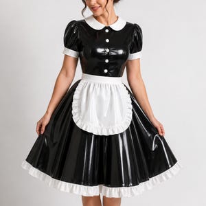 以下が含まれることがあります： 光沢のある仕上げの黒と白のドレス。白い丸襟、白いカフス付きの短いパフスリーブ、フロントボタンのプラケットが特徴です。フリル付きの縁取りがある白いエプロンが、スカートの上のウエスト部分に取り付けられています。