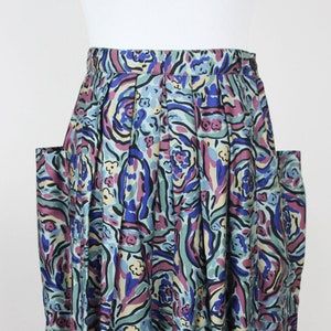 May include: A pleated skirt with a blue, green, and purple abstract floral print. The skirt has two large pockets on the sides.