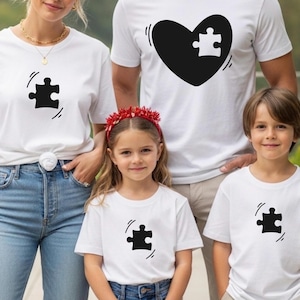 May include: A family wearing matching white t-shirts with a black puzzle piece design. The shirts are worn by two adults and two children. One adult's shirt features a black heart with a puzzle piece.