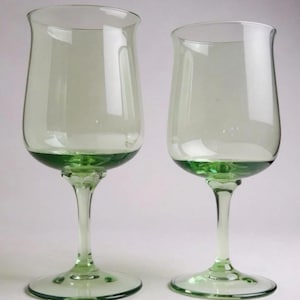 May include: Two clear wine glasses with a green base and stem. The glasses have a tulip-shaped bowl and a wide, rounded rim. The base of each glass is a solid, vibrant green, adding a pop of color to the elegant design. The stem is slender and elegant.