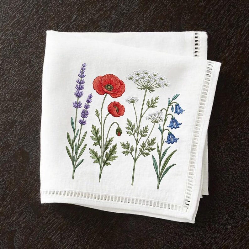 May include: White linen napkin featuring an embroidered floral design. The design includes lavender, red poppies, white Queen Anne's lace, and bluebell flowers. The napkin has a decorative cutwork border.
