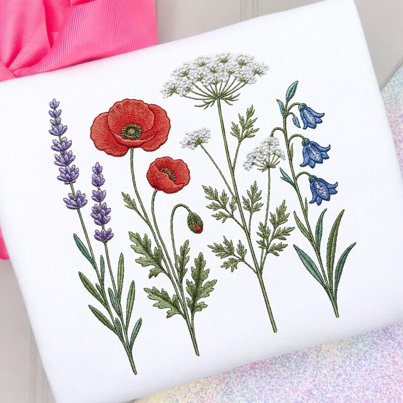 May include: White fabric featuring embroidered wildflowers. The design includes red poppies, lavender, white Queen Anne's lace, and bluebell flowers with green leaves and stems. The embroidery is detailed and colorful, creating a botanical theme.