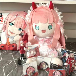 Könnte beinhalten: Eine Sammlung von Anime-Merchandise mit einer pinkhaarigen Figur. Zu den Artikeln gehören eine große Plüschpuppe, ein Kissen, Figuren und mehrere Ansteckbuttons. Das Farbschema ist hauptsächlich rosa, rot und weiß.