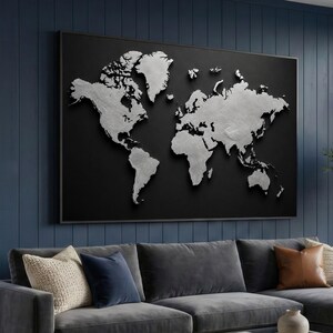Può includere: Una grande opera d'arte incorniciata con una mappa del mondo. La mappa presenta continenti color argento su sfondo nero. L'opera è esposta su una parete blu sopra un divano grigio con cuscini decorativi. La mappa è un elemento decorativo da parete.