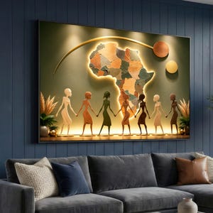 May include: A framed wall art piece featuring a map of Africa with a glowing outline. Below the map, figures of diverse people hold hands. The artwork has a warm color palette with gold accents and is set against a dark teal wall.
