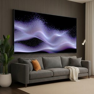 Könnte beinhalten: Großer abstrakter Kunstdruck mit fließenden, geschichteten Wellen in Lila und Weiß vor schwarzem Hintergrund. Das Kunstwerk befindet sich über einem grauen Sofa mit orangefarbenen und grauen Kissen. Eine weiße Decke ist über das Sofa drapiert.