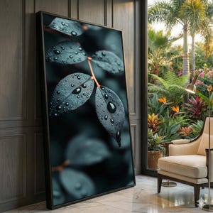 以下が含まれることがあります： 水滴が付いた濃い緑色の葉のクローズアップを特徴とする額入りのアートプリント。葉は質感があり、ぼやけた暗い背景に配置されています。アートワークは木の壁に立てかけられており、窓からは緑豊かな庭が見えます。