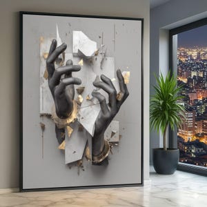 May include: Abstract art print showing two black hands with gold details reaching towards fragmented white and gold geometric shapes. The artwork is framed in black and set against a grey background.