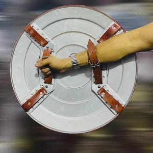 May include: A silver and red shield with brown leather straps and rivets. The shield is round with a silver center and a red border. The straps are attached to the back of the shield.