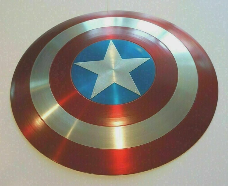 May include: A round shield with a red, silver, and blue color scheme. The shield features a large silver star in the center, surrounded by a blue circle. The outer ring is red, with silver bands separating the colors. The shield is a replica.
