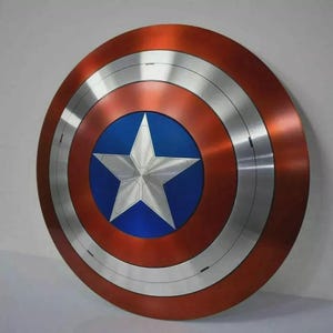 May include: A circular shield with a red, silver, and blue color scheme. The shield features a central blue circle with a white star, surrounded by silver and red concentric rings. The shield has a metallic appearance.