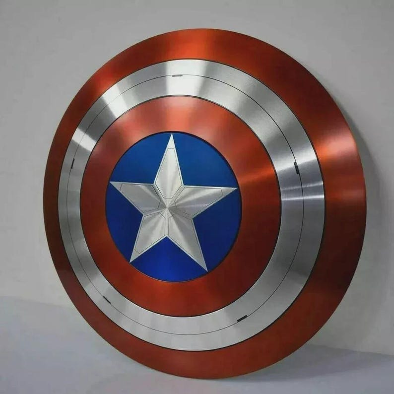 May include: A circular shield with a red, silver, and blue color scheme. The shield features a central blue circle with a white star, surrounded by silver and red concentric rings. The shield has a metallic appearance.