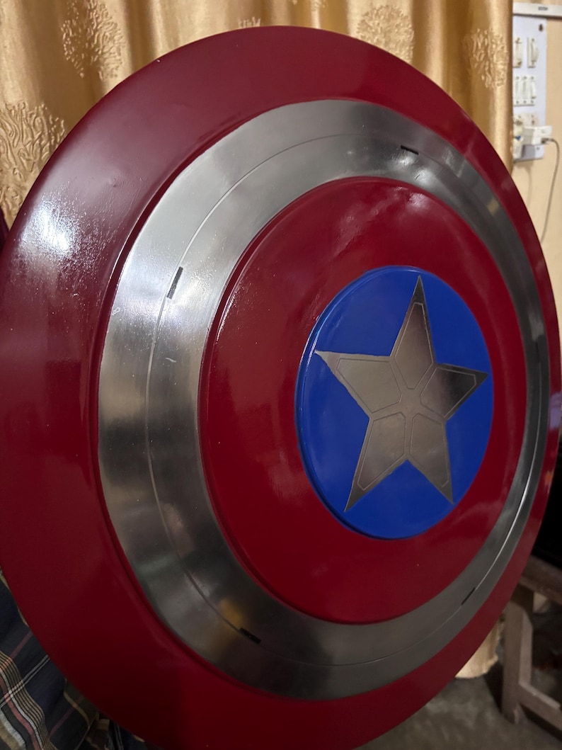 May include: A circular shield featuring a glossy red outer ring, a metallic silver middle ring, and a vibrant blue centre circle. A large, five-pointed silver star is centred within the blue circle, creating a bold, multi-layered design.