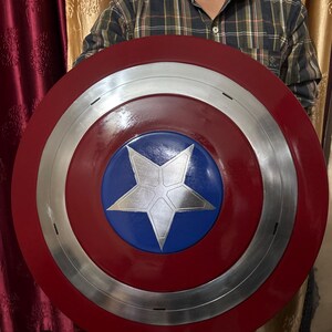 May include: A circular shield featuring a glossy red outer ring, a metallic silver middle ring, and a central blue circle with a large, silver five-pointed star. The design is symmetrical, with clean lines and a polished finish throughout the surface.