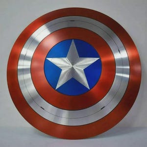 May include: A round shield with a red outer ring, a silver band, and a blue center. A large, five-pointed silver star is centered on the blue circle. The shield has a metallic appearance.
