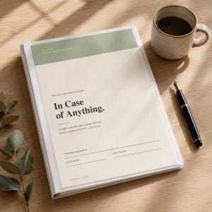 Puede incluir: Un archivador blanco con el texto "In Case of Anything" en la portada, junto a una taza de café y una pluma estilográfica. El archivador está diseñado para guardar información familiar. La portada tiene un acento verde claro.