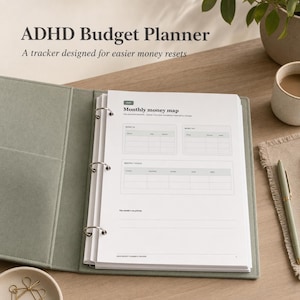 Pode incluir: Um fichário de três argolas verde-sálvia contendo uma folha branca intitulada ADHD Budget Planner. A página apresenta uma seção Monthly money map com tabelas para entradas, saídas e totais, além de uma linha para a prioridade do mês.