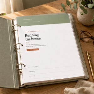 Puede incluir: Una carpeta de tres anillas de color verde salvia que contiene una página blanca con el texto "The Home Management Binder" y "Running the house." La página incluye secciones para "This binder belongs to," "Home address," y "Year started" con detalles en naranja.