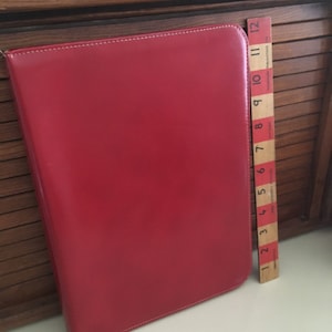 May include: A red leather folder with white stitching. The folder is closed and measures approximately 12 inches in length.