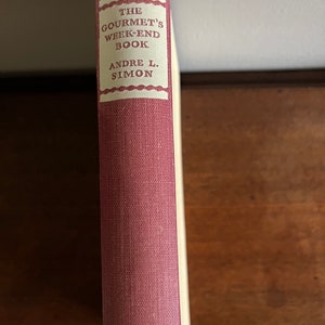 May include: The spine of a red hardcover book titled "The Gourmet's Week-End Book" by Andre L. Simon.