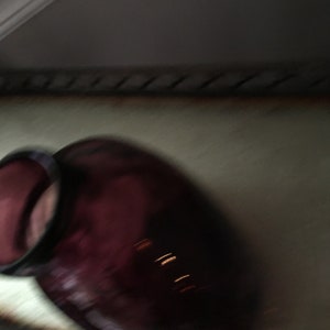Op de afbeelding: Een donkerpaarse glazen fles met een brede opening en een ronde bodem.