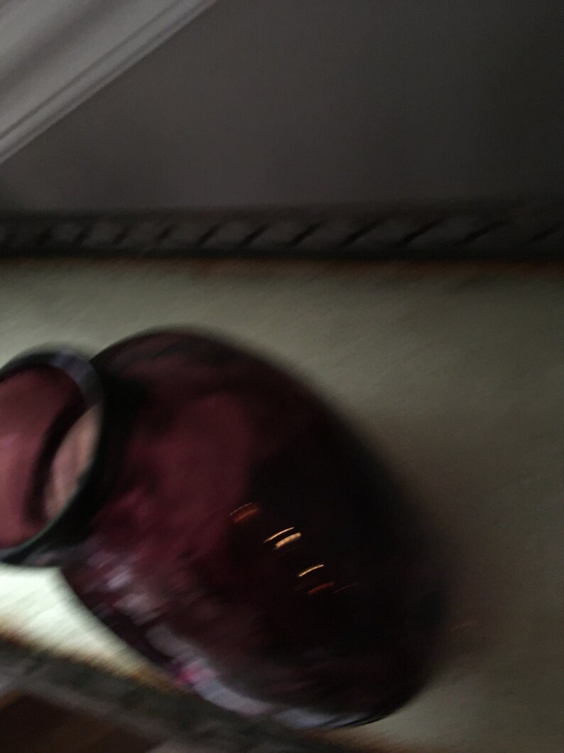 Op de afbeelding: Een donkerpaarse glazen fles met een brede opening en een ronde bodem.